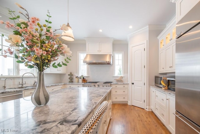 kitchen with ventilation hood, stainless steel appliances, light stone counters, and white cabinetry