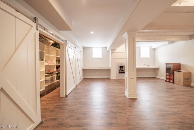 additional living space with a barn door, wood-type flooring, and a healthy amount of sunlight