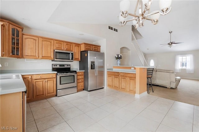 kitchen with decorative light fixtures, a kitchen bar, light tile patterned floors, ceiling fan with notable chandelier, and appliances with stainless steel finishes