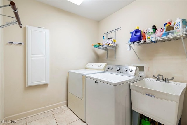 clothes washing area with washing machine and dryer, light tile patterned floors, and sink