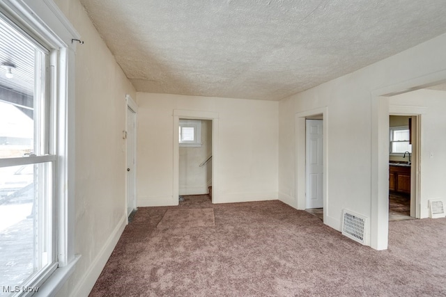 unfurnished bedroom featuring carpet, a textured ceiling, multiple windows, and sink