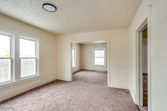 unfurnished room featuring light carpet, plenty of natural light, and a textured ceiling