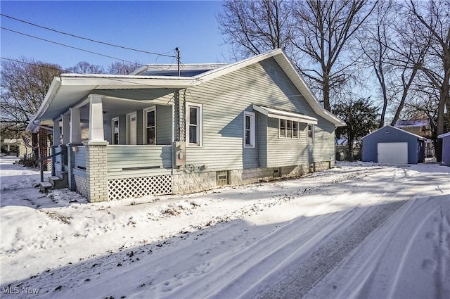 snow covered property featuring an outbuilding, a porch, and a garage