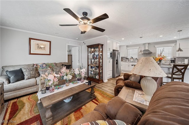 living room with ceiling fan, ornamental molding, a textured ceiling, and light hardwood / wood-style flooring