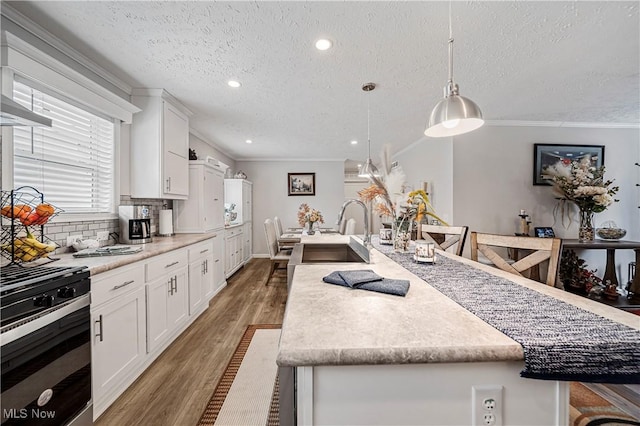 kitchen with pendant lighting, a center island with sink, white cabinets, a textured ceiling, and range