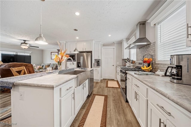 kitchen with stainless steel appliances, sink, wall chimney range hood, hanging light fixtures, and an island with sink