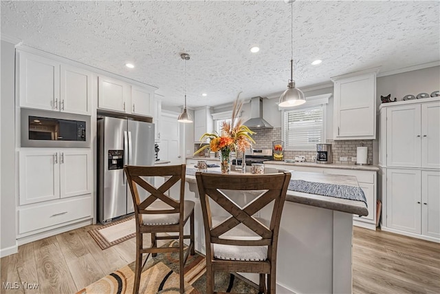 kitchen featuring stainless steel refrigerator with ice dispenser, wall chimney exhaust hood, white cabinets, a center island, and hanging light fixtures