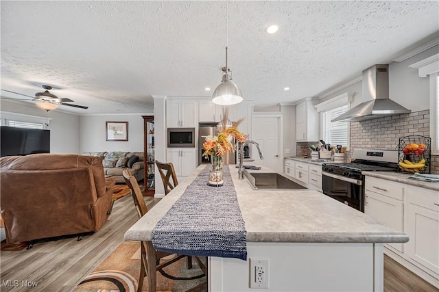 kitchen featuring sink, wall chimney exhaust hood, hanging light fixtures, stainless steel appliances, and tasteful backsplash