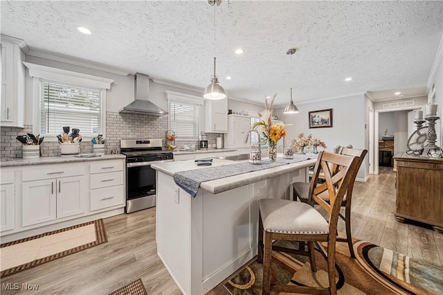 kitchen featuring white cabinets, sink, wall chimney exhaust hood, stainless steel range, and decorative light fixtures