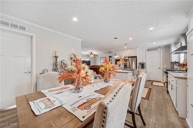 dining space with ceiling fan, light hardwood / wood-style flooring, a textured ceiling, and ornamental molding