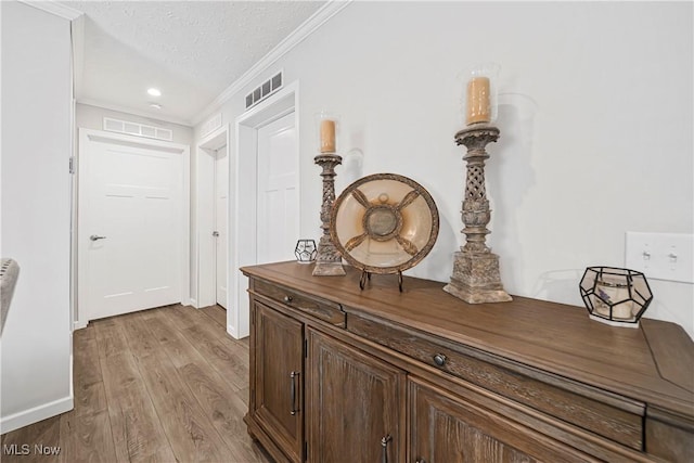 hallway with crown molding, light wood-type flooring, and a textured ceiling