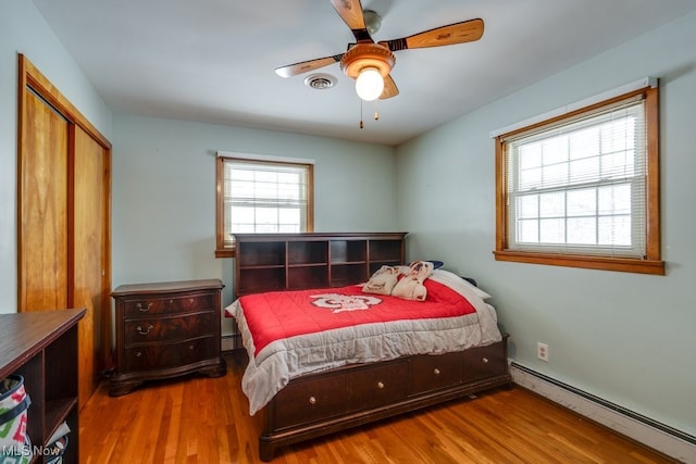 bedroom with a closet, visible vents, a baseboard heating unit, and wood finished floors