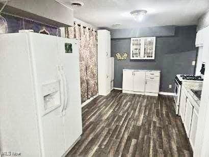 kitchen with white cabinets, stove, white refrigerator with ice dispenser, and dark wood-type flooring