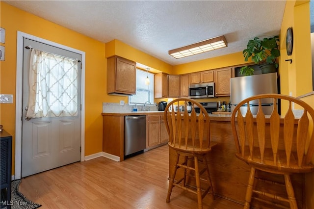 kitchen with sink, light hardwood / wood-style floors, a textured ceiling, and appliances with stainless steel finishes