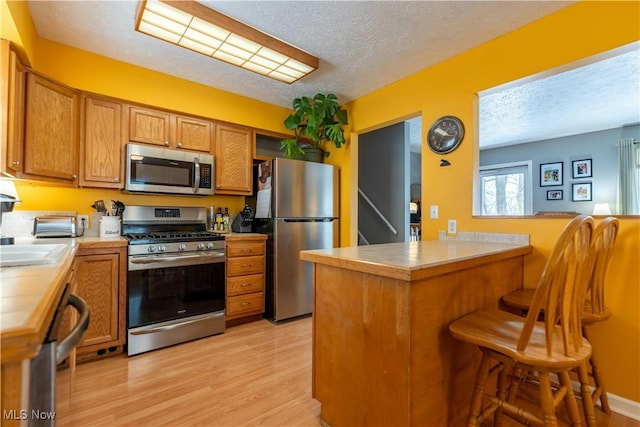 kitchen with a kitchen breakfast bar, light hardwood / wood-style flooring, a textured ceiling, kitchen peninsula, and stainless steel appliances