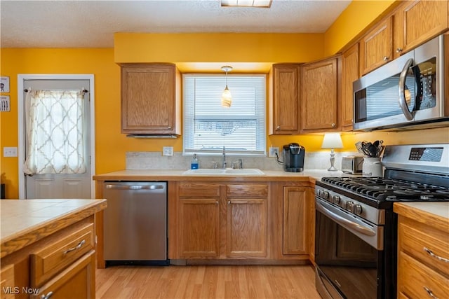 kitchen with light wood-type flooring, a textured ceiling, stainless steel appliances, sink, and decorative light fixtures