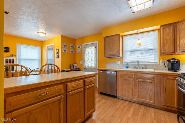 kitchen featuring sink, light hardwood / wood-style floors, pendant lighting, a textured ceiling, and appliances with stainless steel finishes