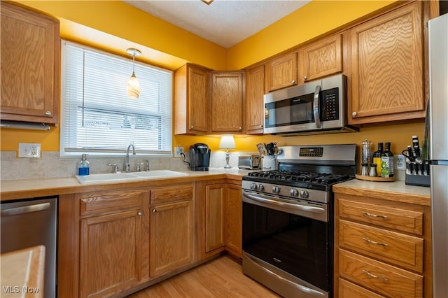 kitchen featuring hanging light fixtures, sink, light hardwood / wood-style flooring, a textured ceiling, and appliances with stainless steel finishes