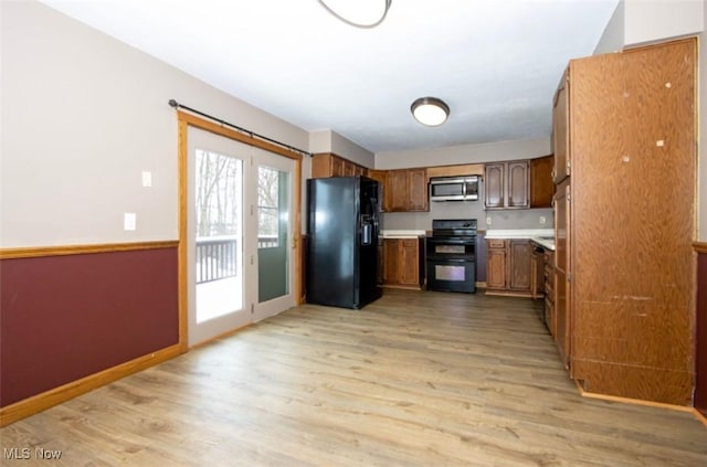 kitchen with light wood finished floors, light countertops, brown cabinetry, black appliances, and baseboards