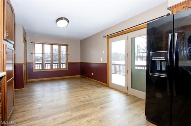 doorway to outside featuring light wood finished floors and wainscoting