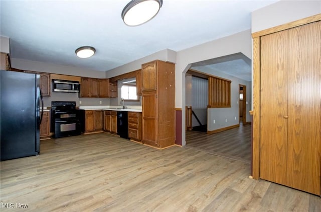 kitchen with arched walkways, light wood-style flooring, a sink, light countertops, and black appliances