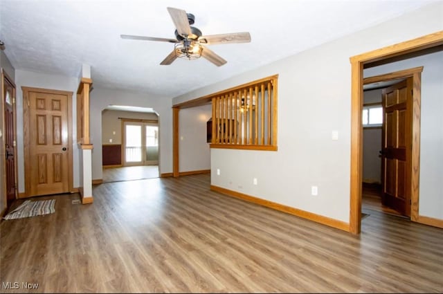 unfurnished living room with a ceiling fan, baseboards, arched walkways, and wood finished floors