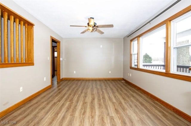 empty room with light wood finished floors, a ceiling fan, and baseboards