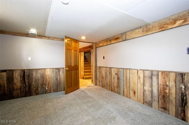 carpeted spare room featuring stairs, wooden walls, and wainscoting