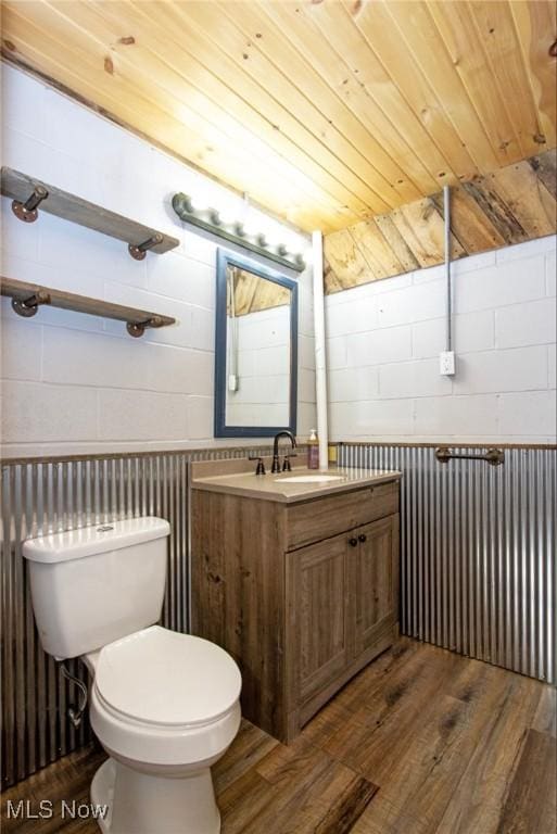 half bathroom featuring concrete block wall, wood ceiling, toilet, and wood finished floors