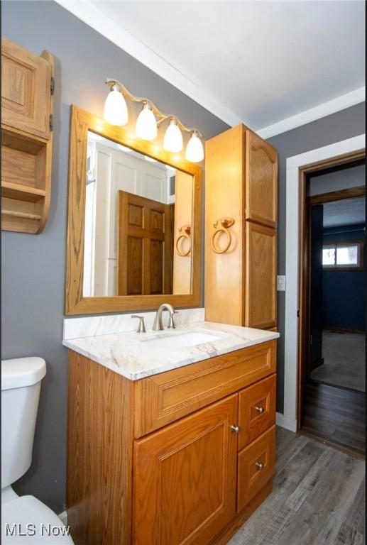 bathroom featuring toilet, ornamental molding, wood finished floors, and vanity