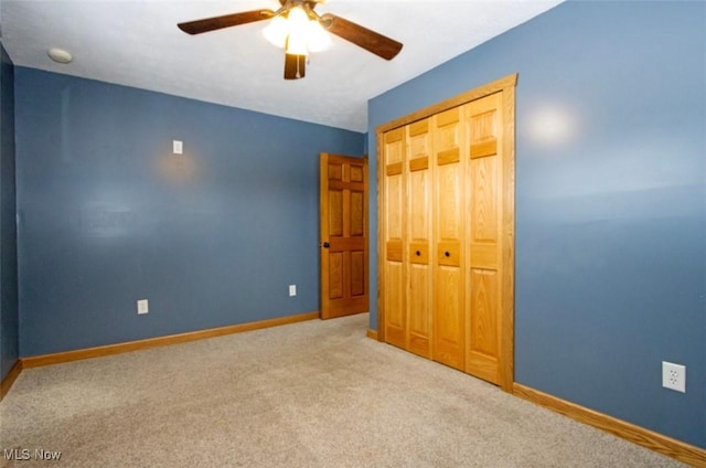 unfurnished bedroom featuring carpet floors, a closet, baseboards, and a ceiling fan