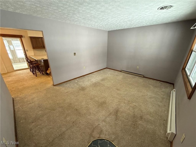 empty room with a textured ceiling, light colored carpet, and baseboard heating