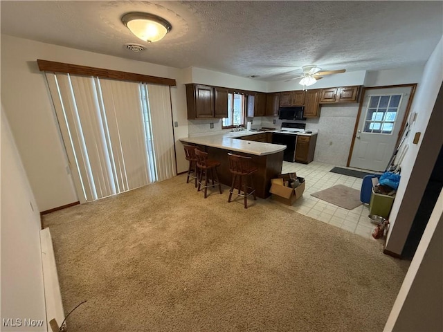 kitchen featuring a kitchen breakfast bar, sink, white electric stove, ceiling fan, and a textured ceiling