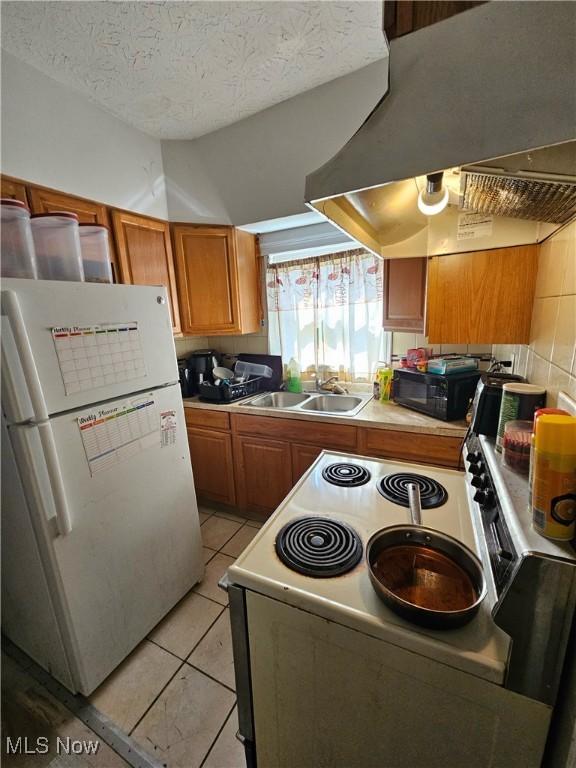 kitchen featuring white appliances, a textured ceiling, island exhaust hood, sink, and light tile patterned floors