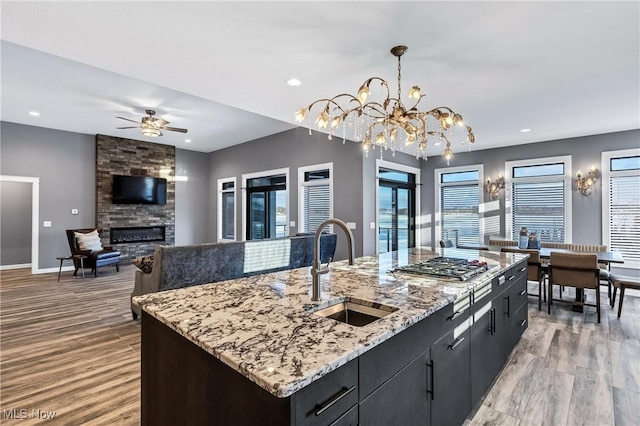 kitchen with pendant lighting, sink, a fireplace, light hardwood / wood-style floors, and an island with sink