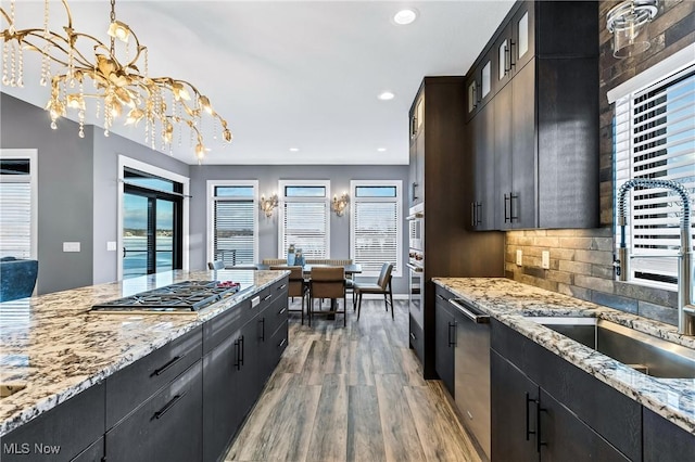 kitchen with sink, tasteful backsplash, decorative light fixtures, stainless steel appliances, and light hardwood / wood-style floors