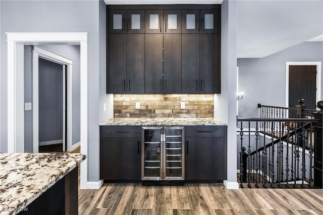 kitchen with hardwood / wood-style floors, dark brown cabinetry, light stone countertops, decorative backsplash, and beverage cooler