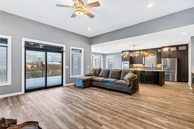 living room featuring sink, ceiling fan with notable chandelier, and light hardwood / wood-style flooring