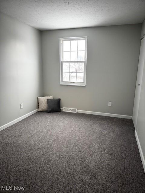 empty room with dark colored carpet and a textured ceiling