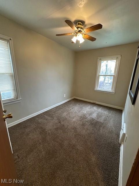 spare room with ceiling fan and dark carpet