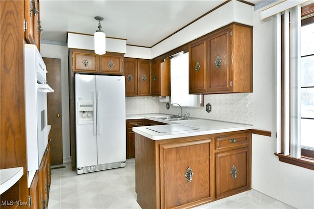 kitchen with kitchen peninsula, a wealth of natural light, sink, white refrigerator with ice dispenser, and hanging light fixtures