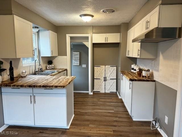 kitchen featuring wooden counters, sink, a textured ceiling, dark hardwood / wood-style flooring, and white cabinetry