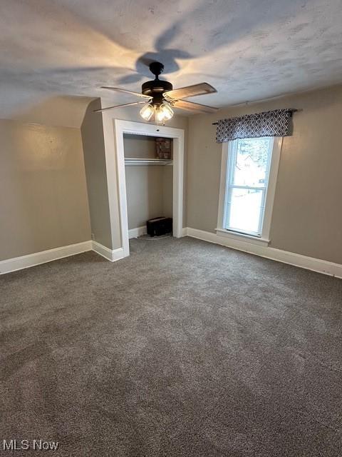 unfurnished bedroom with a closet, dark carpet, ceiling fan, and lofted ceiling