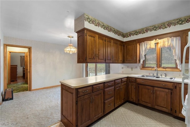 kitchen featuring kitchen peninsula, light colored carpet, hanging light fixtures, and sink