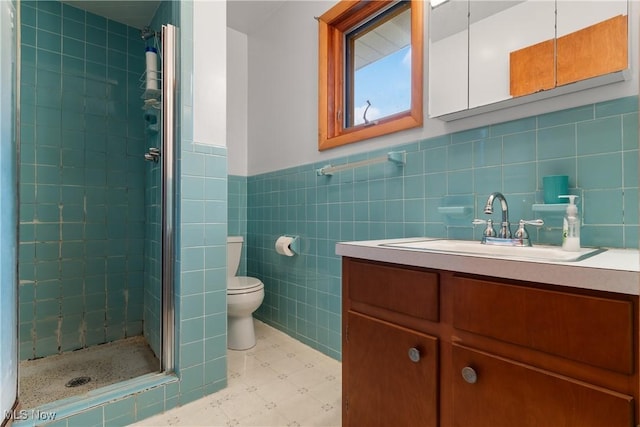 bathroom with vanity, toilet, a shower with shower door, and tile walls