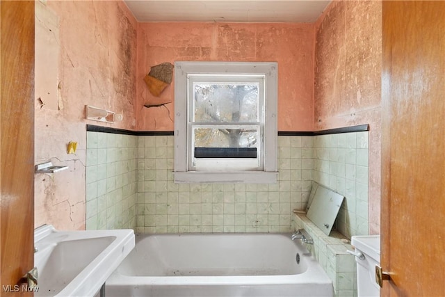 bathroom featuring a bath, toilet, tile walls, and sink