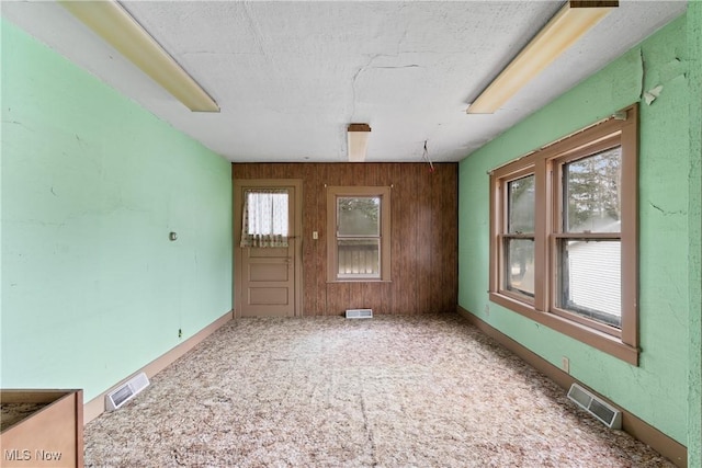 carpeted spare room with a textured ceiling and wooden walls