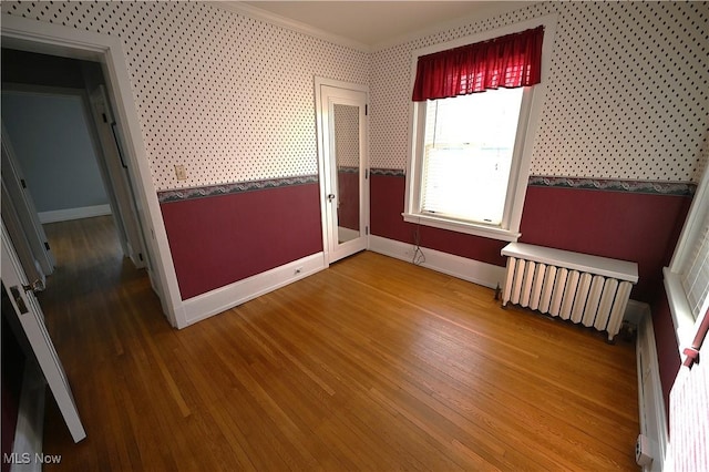 unfurnished bedroom with hardwood / wood-style floors, a baseboard heating unit, radiator, and ornamental molding