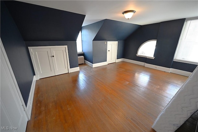 additional living space with radiator, wood-type flooring, and vaulted ceiling