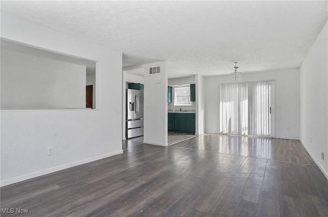 unfurnished living room with a chandelier, a textured ceiling, dark hardwood / wood-style flooring, and sink